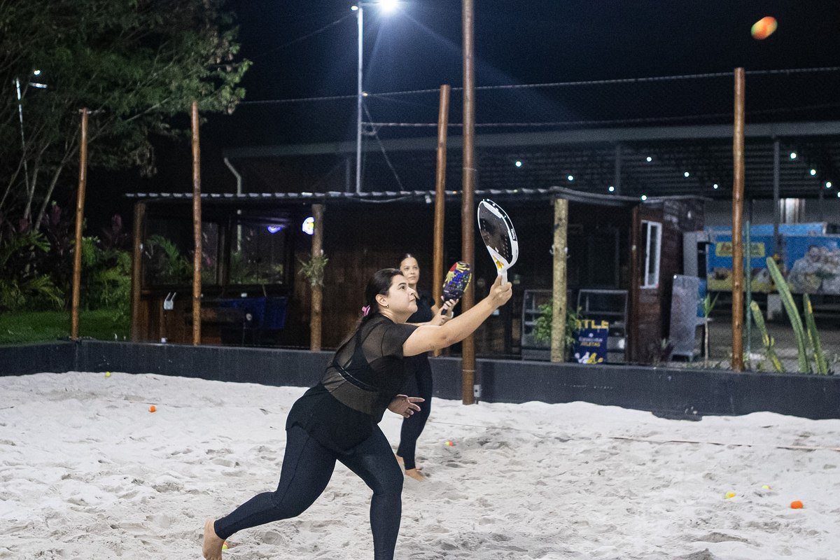 Aluna jogando beach tennis sob a iluminação da arena