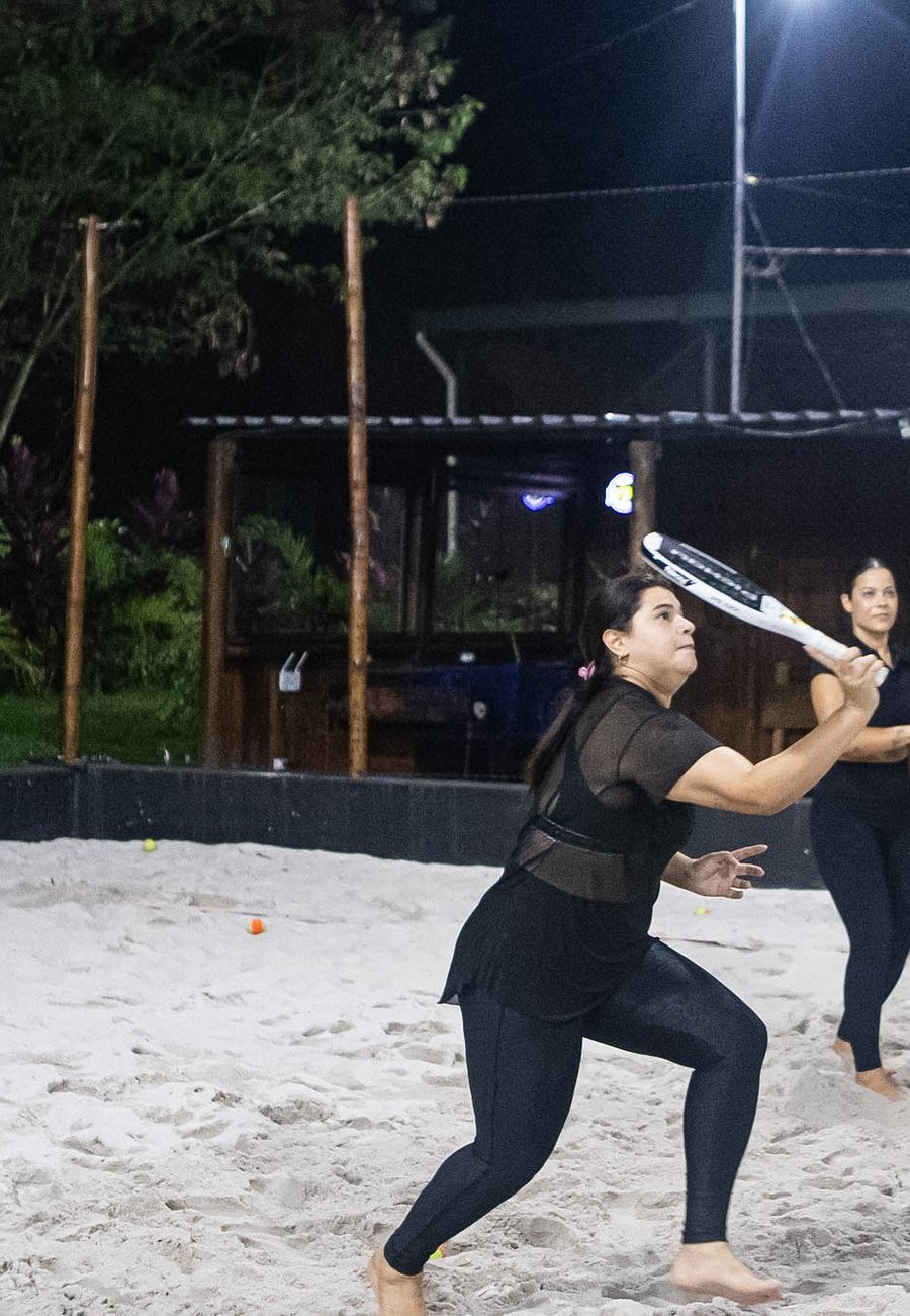 Aluna devolvendo a bola em aula de beach tennis à noite
