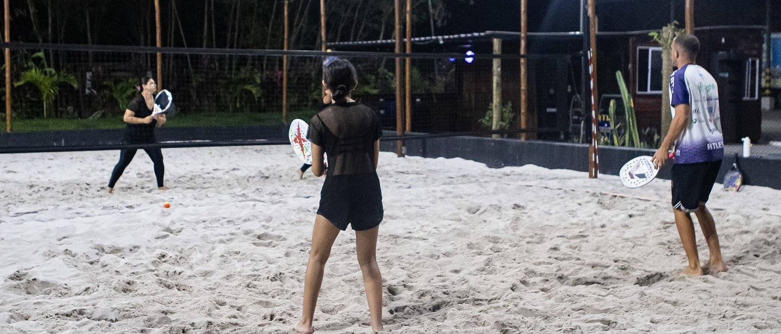Quadra de areia da Still Fit Xerém iluminada à noite, com alunos jogando